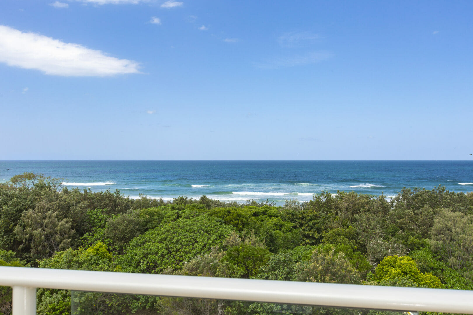 balcony view of ocean waves and foreshore tree tops