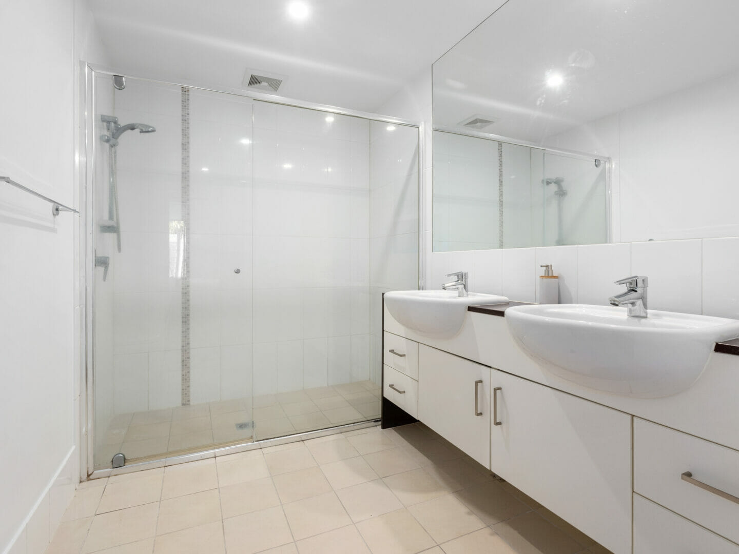 Bathroom vanity with double basins next to a glass shower enclosure