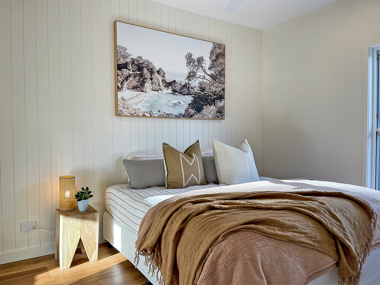 King sized bed with lots of pillows, a beach themed print on the wall.